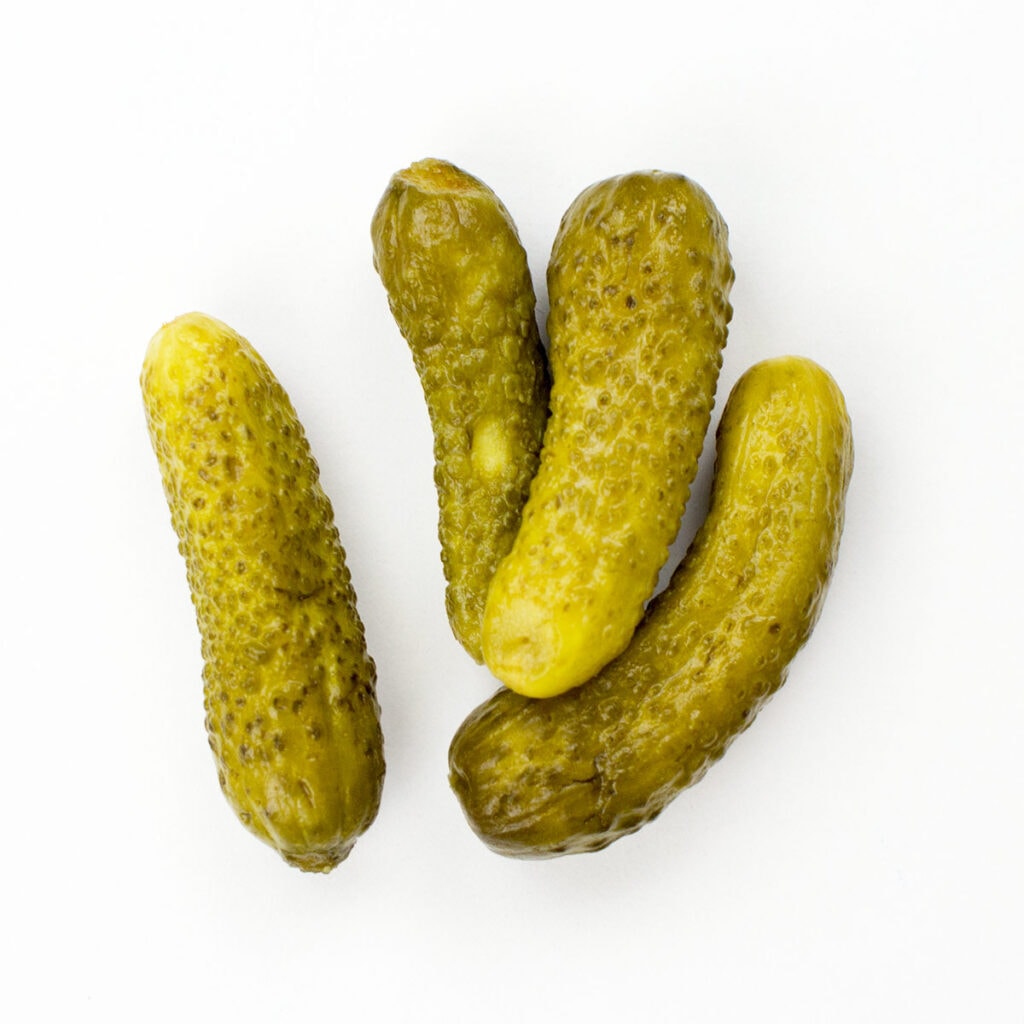 Four gherkins on white surface
