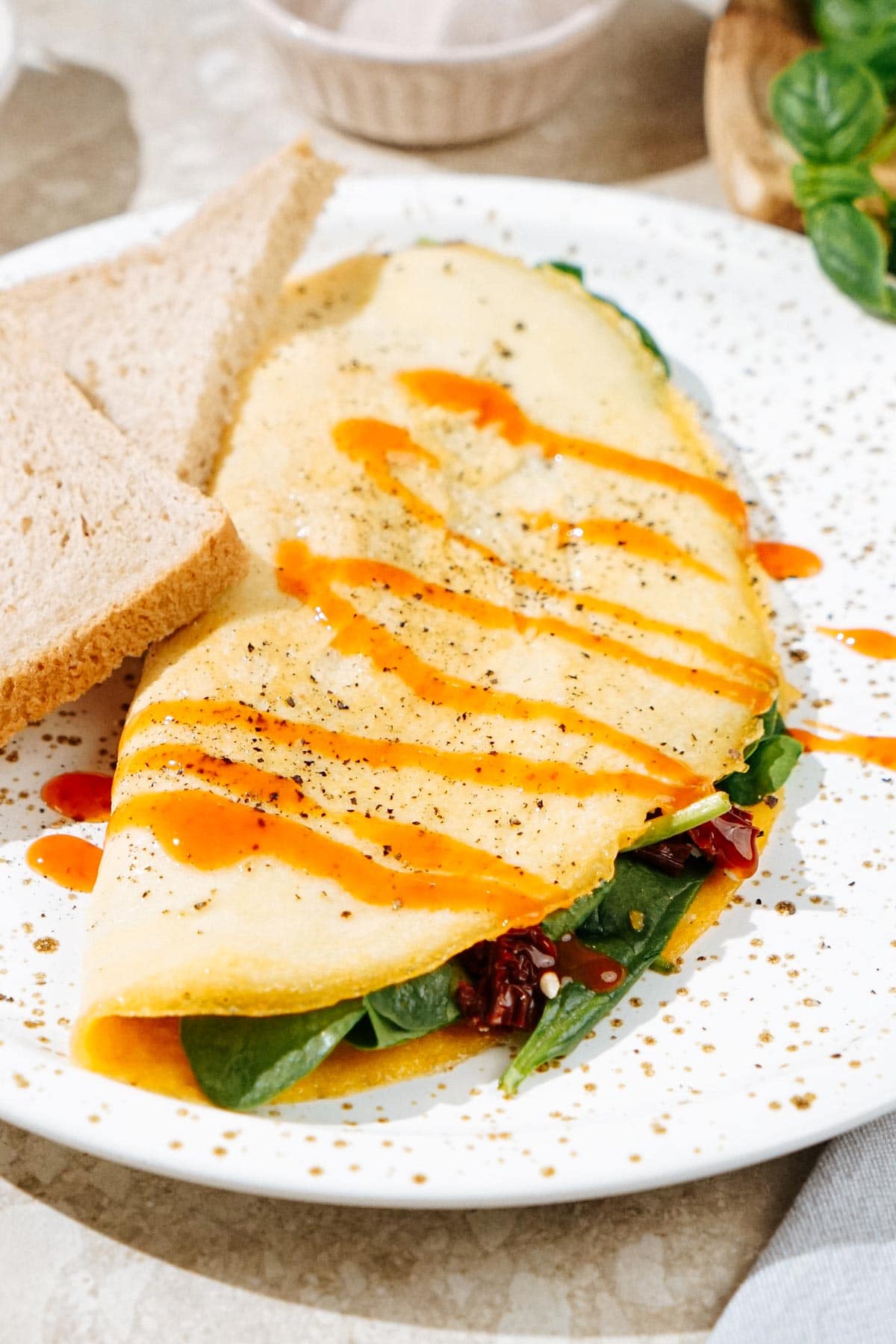 High Protein Omelette, topped with sriracha, salt and black pepper which is on the light plate. Two pieces of bread are on it as well | Hurry The Food Up