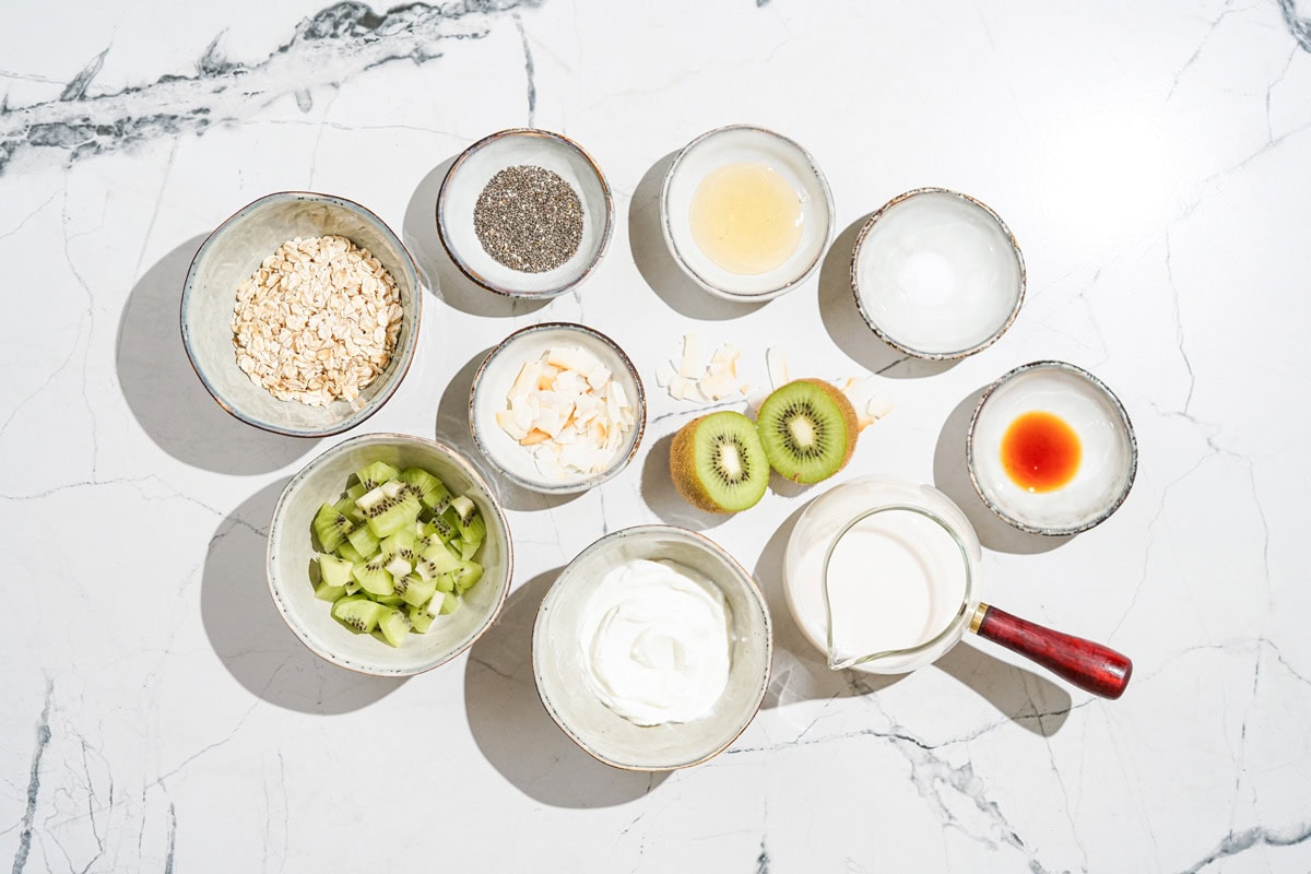 High-protein overnight oats ingredients like rolled oats, chia seeds, honey, soy milk, Greek yogurt, kiwi, coconut flakes etc | Hurry The Food Up