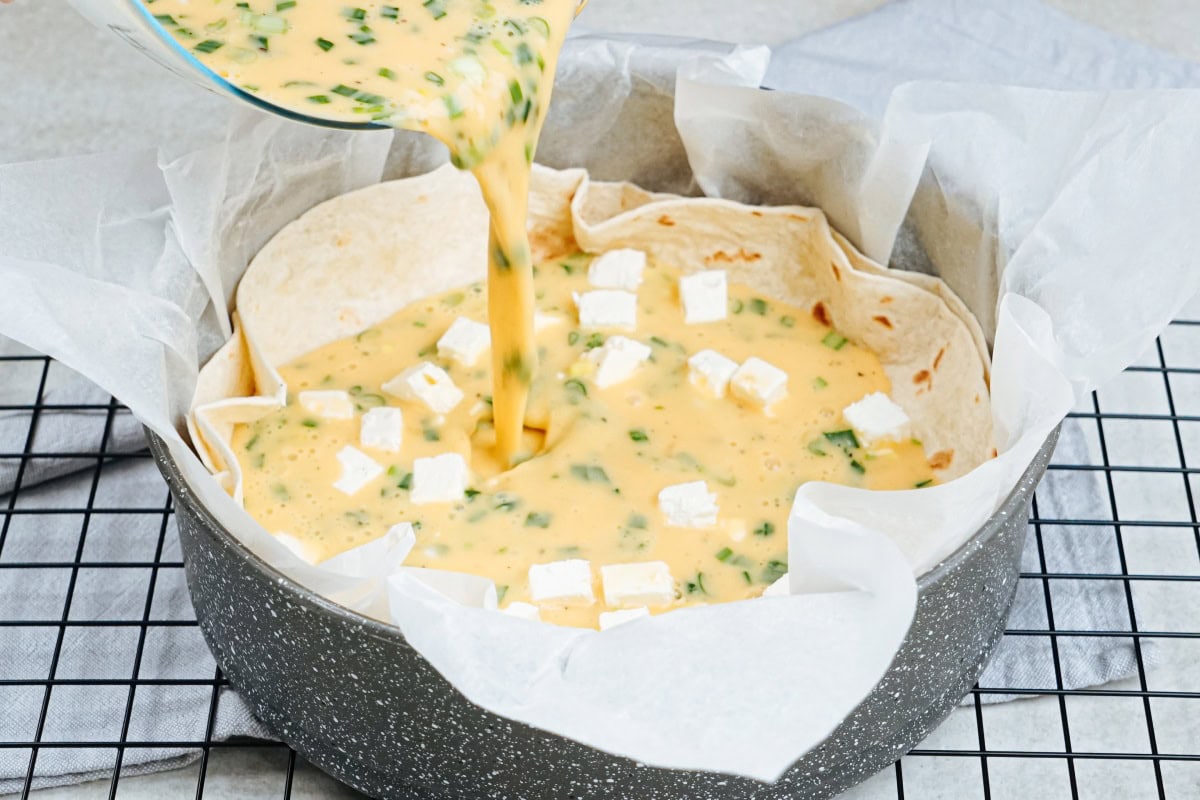 The process of pouring the egg mixture over the cheese-layered tortillas | Hurry The Food Up