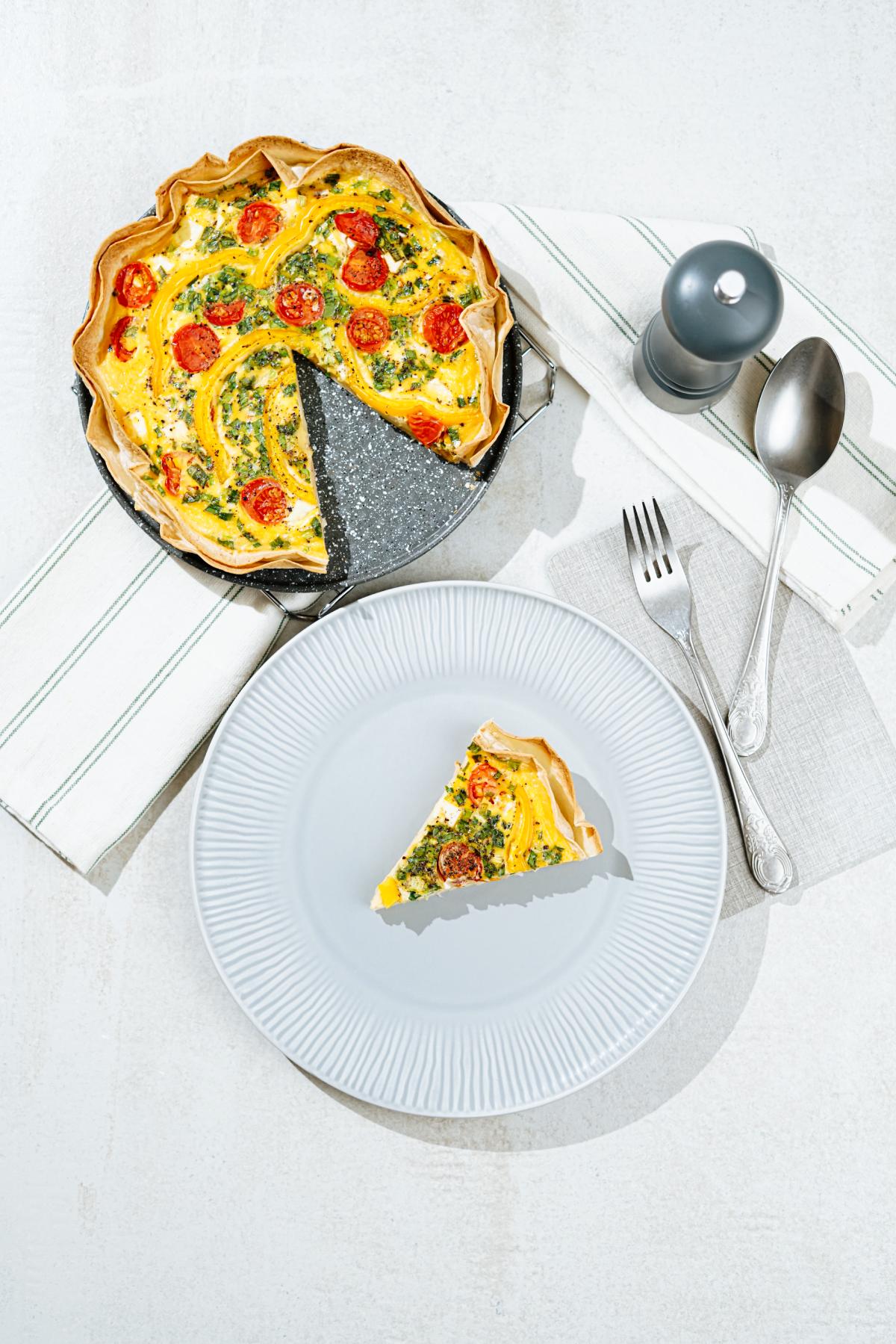 Bird's-eye view of the plate with tortilla quiche's piece. The fork, spoon, kitchen towel, salt grinder, and the black plate with tortilla quiche surround it | Hurry The Food Up