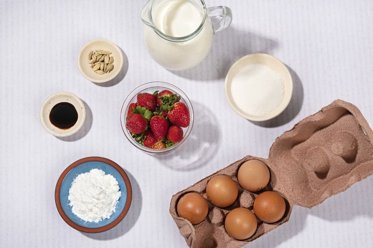 A jar of milk, 5 eggs, some strawberries, cardamom seeds, cornflour, sugar and syrup on a grey surface | Hurry The Food Up