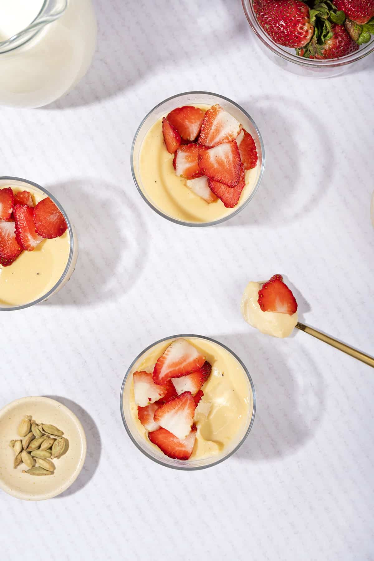 A birds eye view of custard with strawberries in ramekins. A teaspoon of custard has been scooped out | Hurry The Food Up