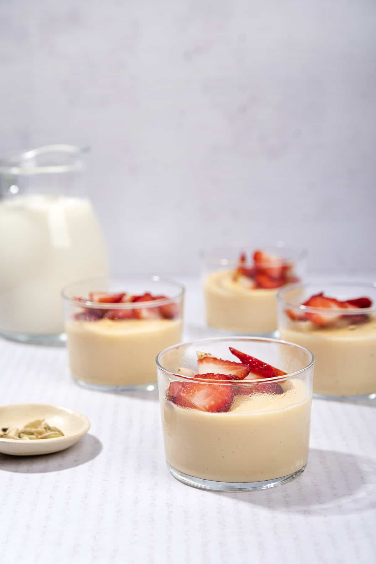 4 ramekins of custard topped with chopped strawberries on a table. A Jug of milk is in the background. | Hurry The Food Up