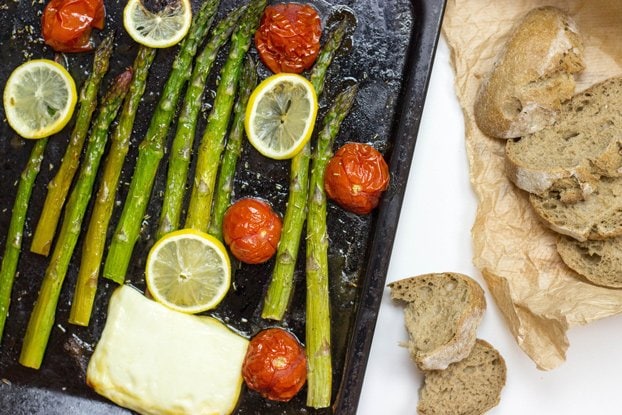 Roasted asparagus, tomato, halloumi and lemon are laid on the baking tray that is on the table with slices of bread | Hurry The Food Up