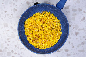 There is a blue skillet with roast corn kernels on the table | Hurry The Food Up