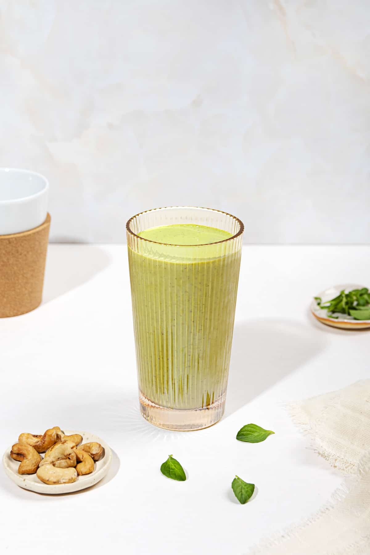 A tall glass of smoothie with torn mint leaves next to it and two small trays, of cashews & mint | Hurry The Food Up