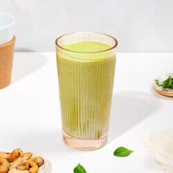 A tall glass of smoothie with torn mint leaves next to it and two small trays, of cashews & mint | Hurry The Food Up