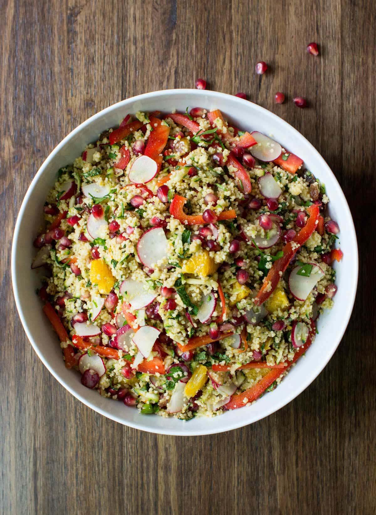 A big white bowl of colourful vegan Moroccan couscous salad is on a dark wooden surface. | Hurry The Food Up