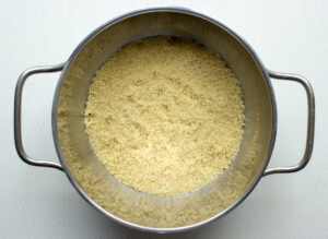 A saucepan full of couscous on a white surface, ready to be used in the vegan moroccan couscous salad. | Hurry The Food Up
