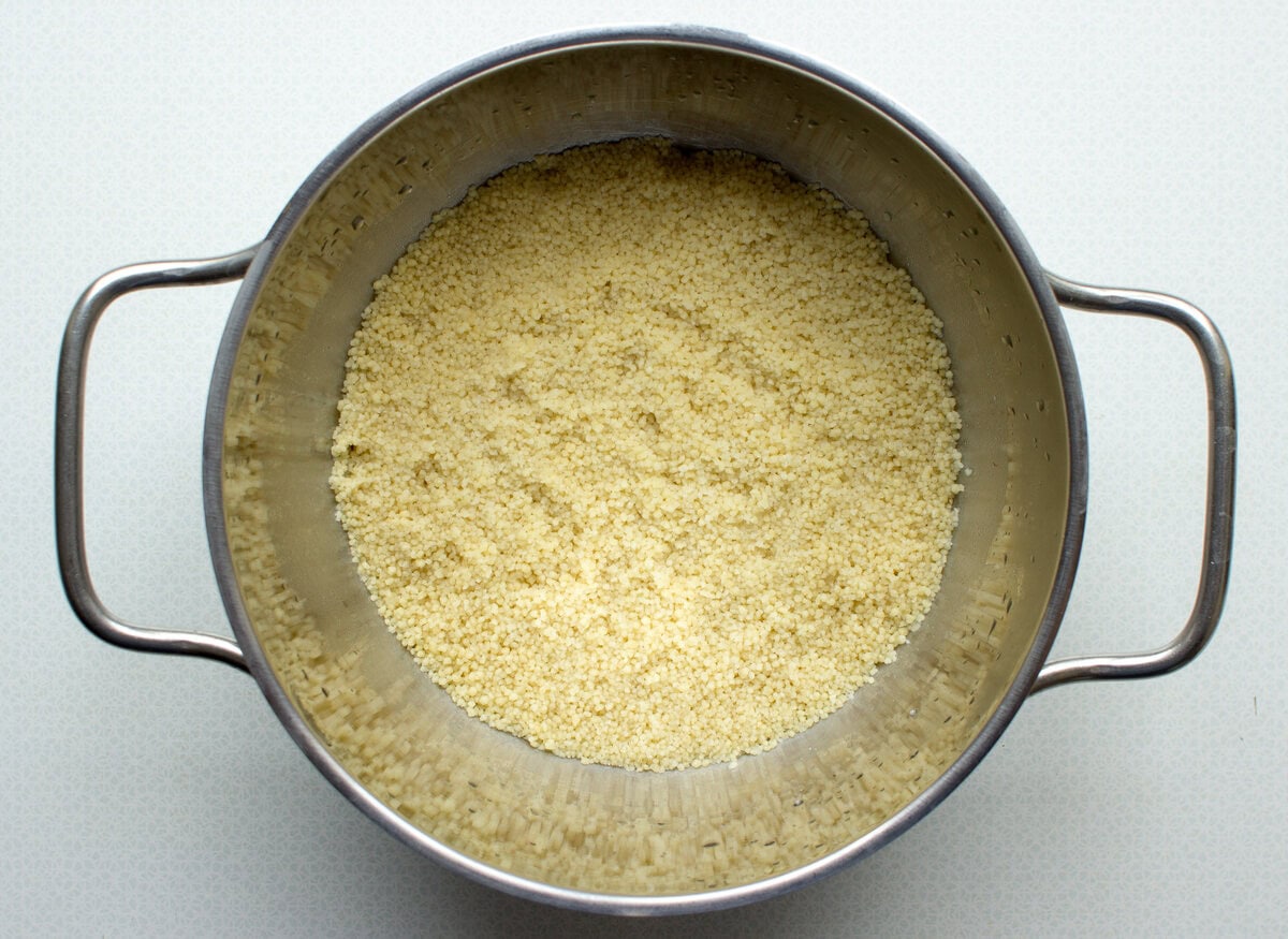 A saucepan full of couscous on a white surface, ready to be used in the vegan moroccan couscous salad. | Hurry The Food Up
