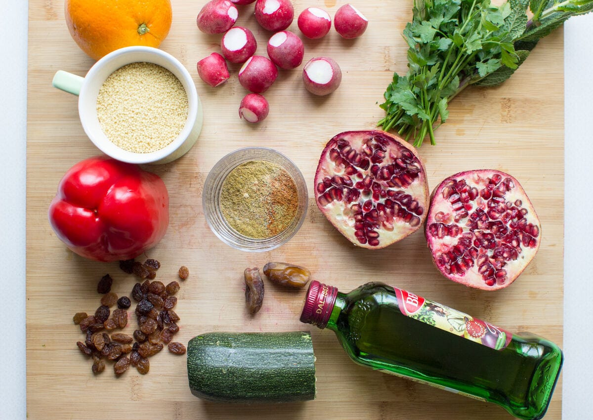 Ingredients for a moroccan couscous salad are laid out on a wooden surface, including a pomegranate | Hurry The Food Up