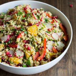 A big white bowl of colourful vegan Moroccan couscous salad is on a dark wooden surface. | Hurry The Food Up