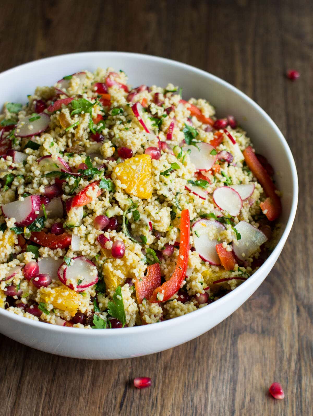 A big white bowl of colourful vegan Moroccan couscous salad is on a dark wooden surface. | Hurry The Food Up