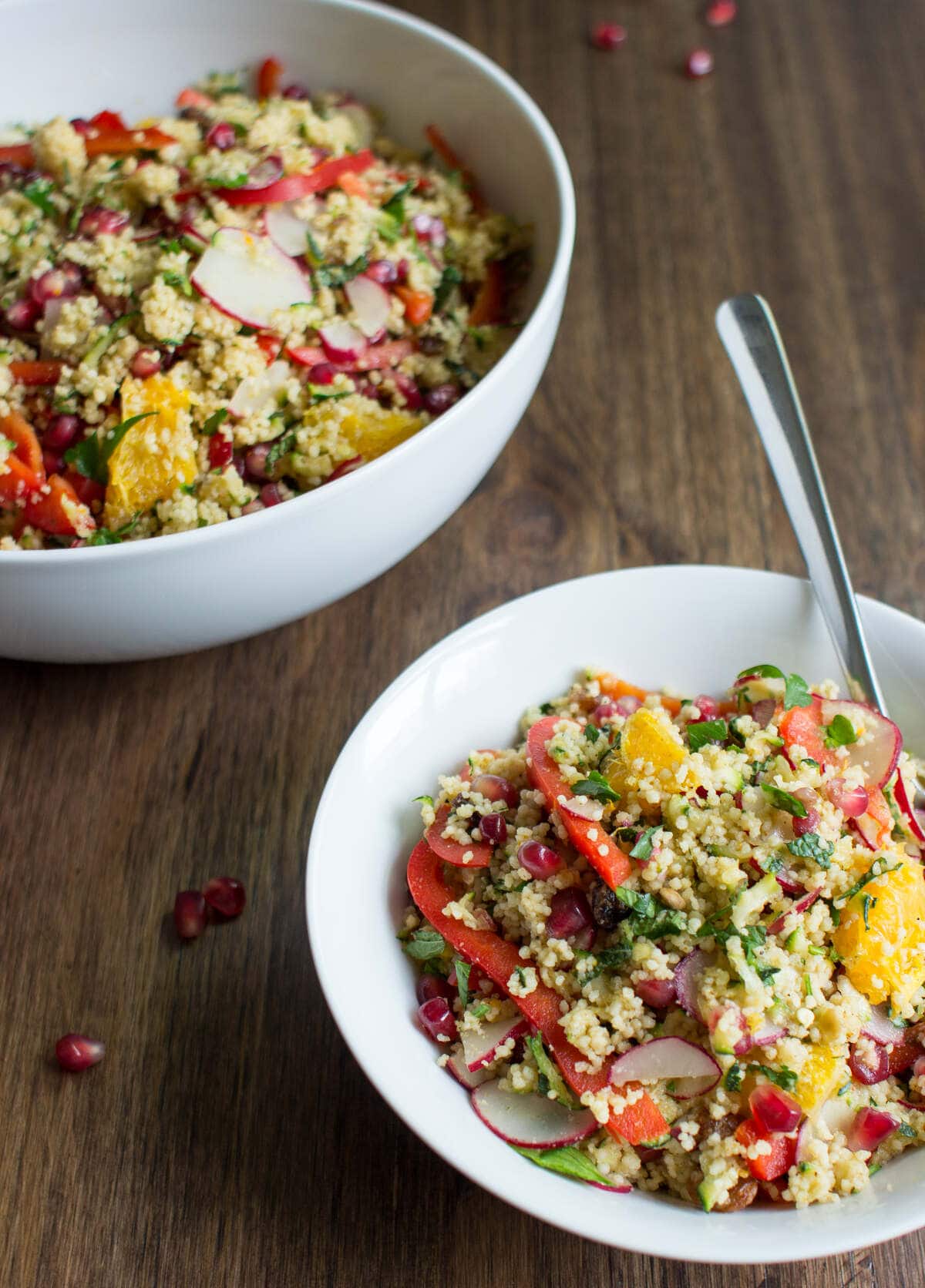 A big bowl of moroccan couscous salad and a smaller bowl with a spoon in it, on a wooden surface. | Hurry The Food Up