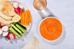 A birds eye view of a bowl with muhammara dip, a plate with vegetables and flatbreads, a glass of water and a tea towel | Hurry The Food Up