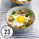 Two bowls of Mushroom Oeuf Cocotte, baked with vegetables and garnished with herbs, rest on a striped cloth inside a glass tray with a timestamp in the left corner.