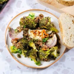 The Oven Roasted Broccoli Halloumi is served on a white plate next to the baking tray and wooden board with bread slices | Hurry The Food Up