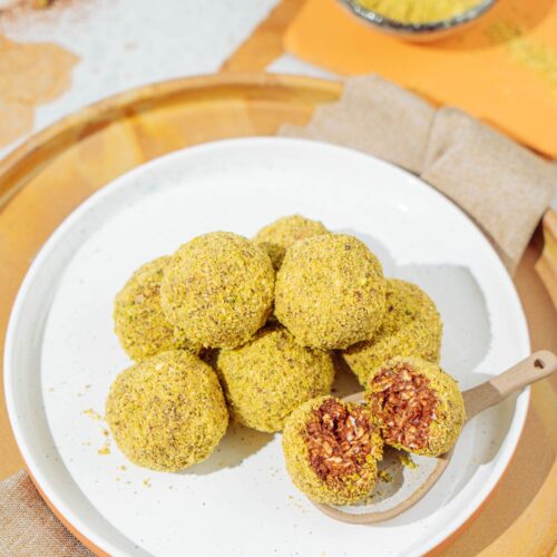 A white plate with peanut butter protein balls that is is on the wooden tray with linen napkin under it. Near it there is a small bowl with ground nuts | Hurry The Food Up