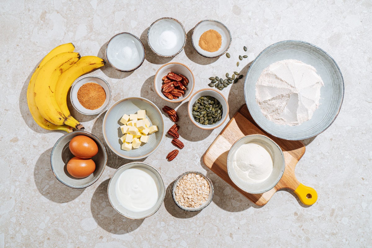 Protein banana bread ingredients like butter, bananas, protein powder, vanilla, rolled oats, greek yogurt, eggs, brown sugar, wholemeal flour, salt, cinnamon, pumpkin seeds, pecans | Hurry The Food Up