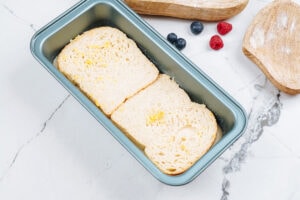 Some slices of bread are in the loaf tin. Near it, there are some wooden dishes and berries | Hurry The Food Up