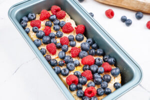 Protein French toast with fruits on the top lie in the loaf tin. Next to it, there are some berries and wooden dishes | Hurry The Food Up