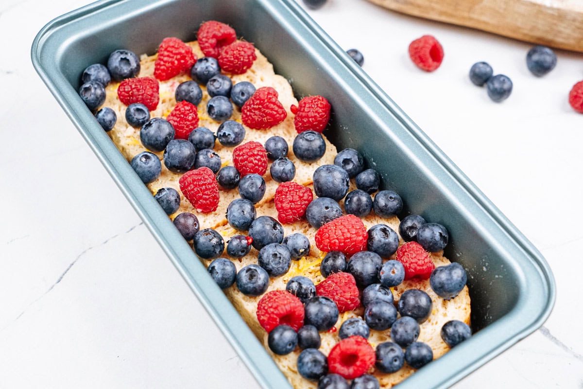 Protein French toast with fruits on the top lie in the loaf tin. Next to it, there are some berries and wooden dishes | Hurry The Food Up