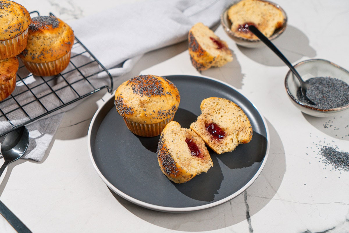 Protein muffins are on the dark plate. Near it there are some whole muffins on a metal grid and a small bowl with poppy seeds etc | Hurry The Food Up
