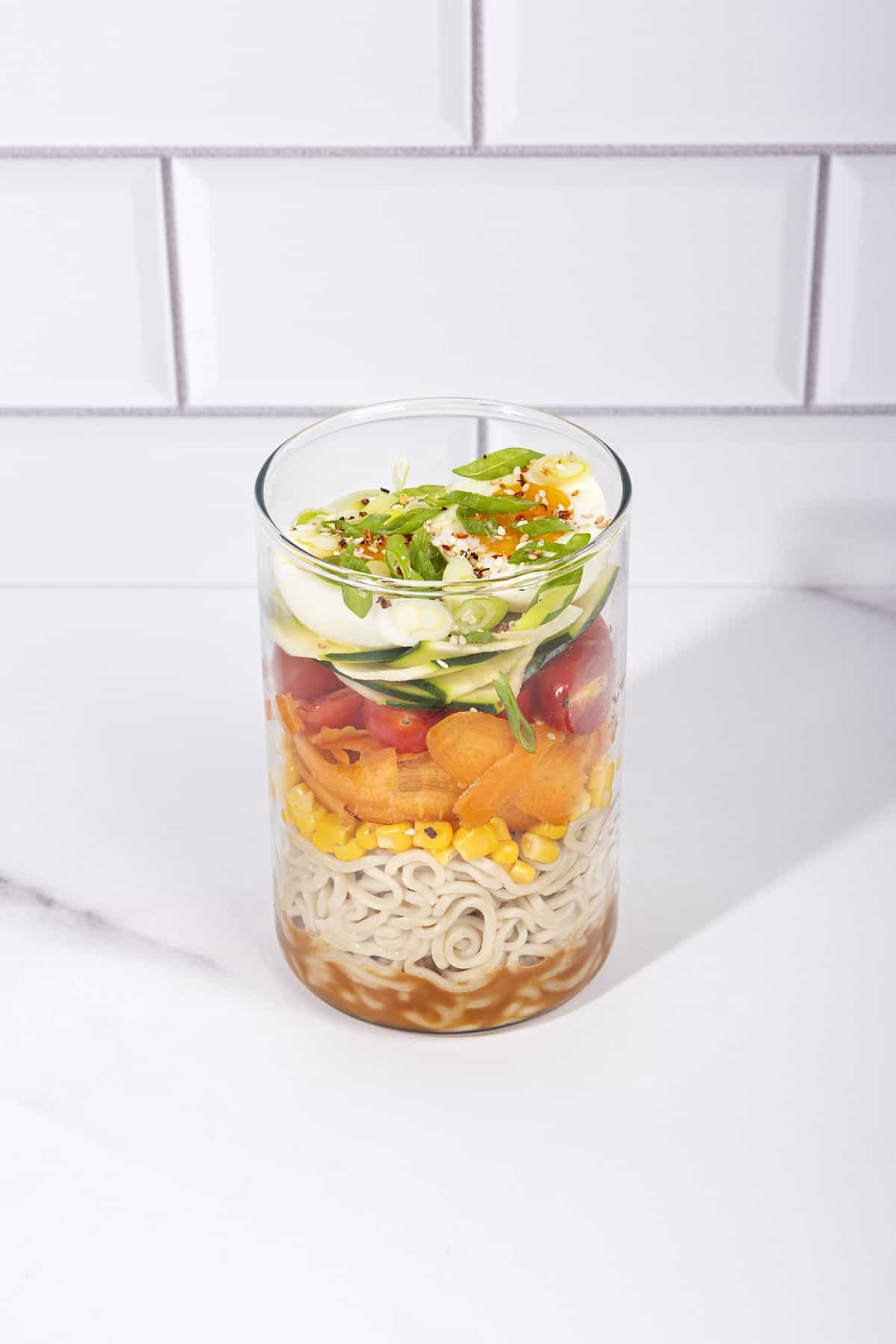 A jar with layers of salad ingredients - seasoning, noodles, corn, carrots, tomatoes, egg, spring onion | Hurry The Food Up