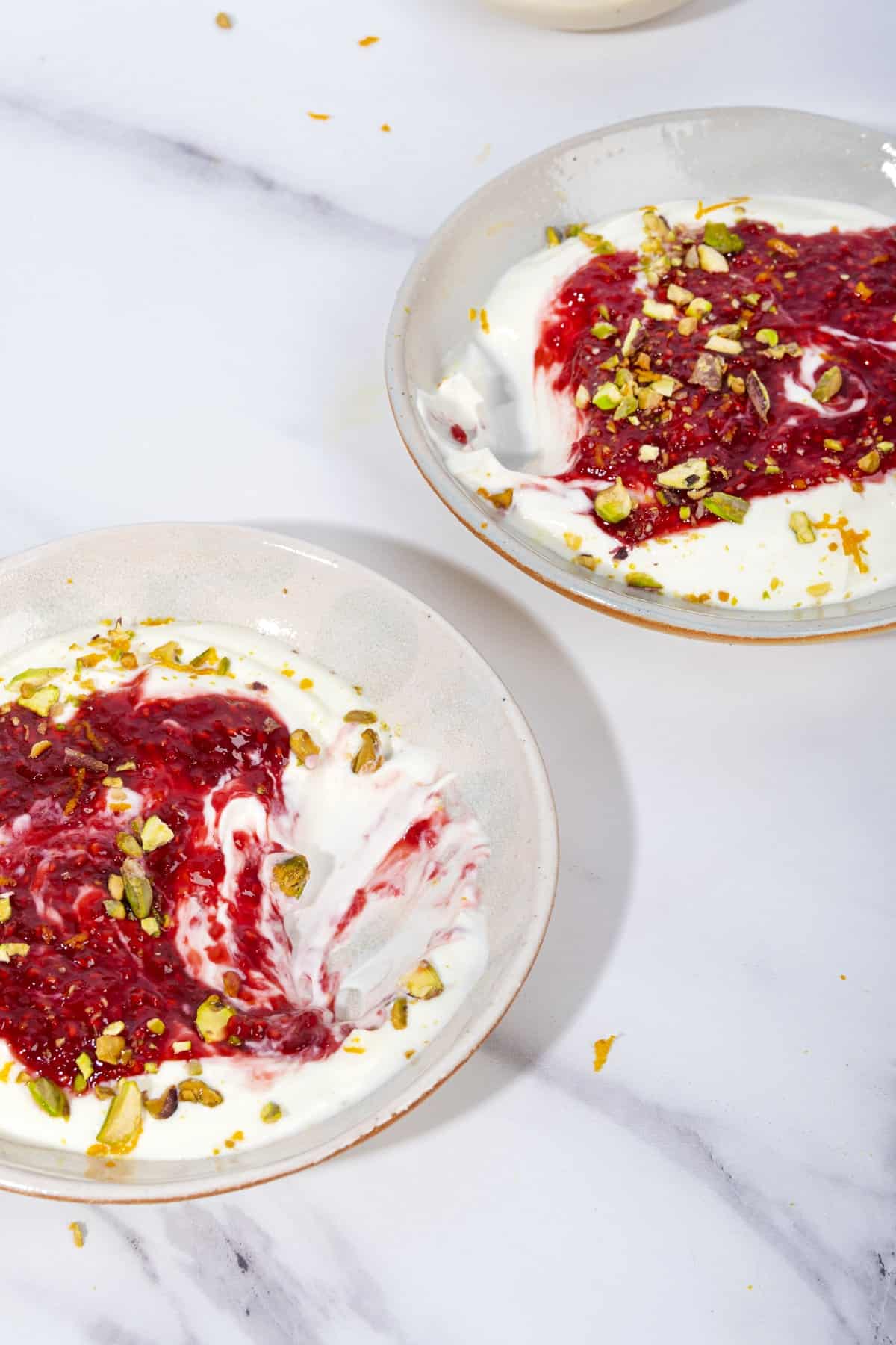 Two bowls of yogurt and raspberry compote on a marble surface. A scoop has been taken out of each bowl | Hurry The Food Up