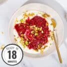 A white bowl of yogurt, compote and pistachios, with a golden spoon in it, on a marble surface with a time stamp in the bottom left hand corner | Hurry The Food Up