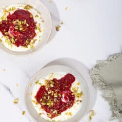 Two bowls of yogurt with compote, sprinkled with pistachios. A small bowl of pistachios in the corner | Hurry The Food Up