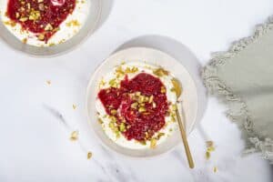 2 white bowls of yogurt, compote and pistachios, one with a golden spoon in it, on a marble surface. | Hurry The Food Up