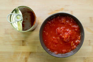 There is a plate with tomato pasta and empty tin of it on the wooden surface | Hurry The Food Up