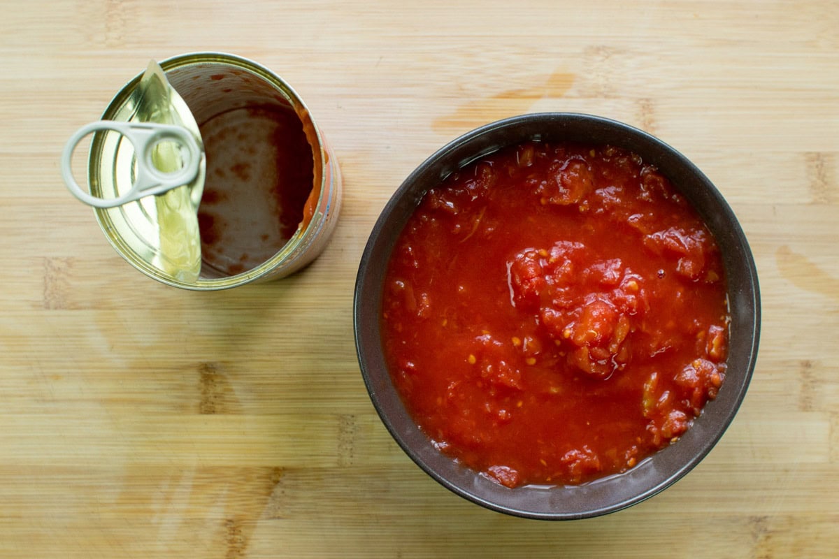 A brown bowl with tomato pasta and empty tin of it on the wooden surface | Hurry The Food Up