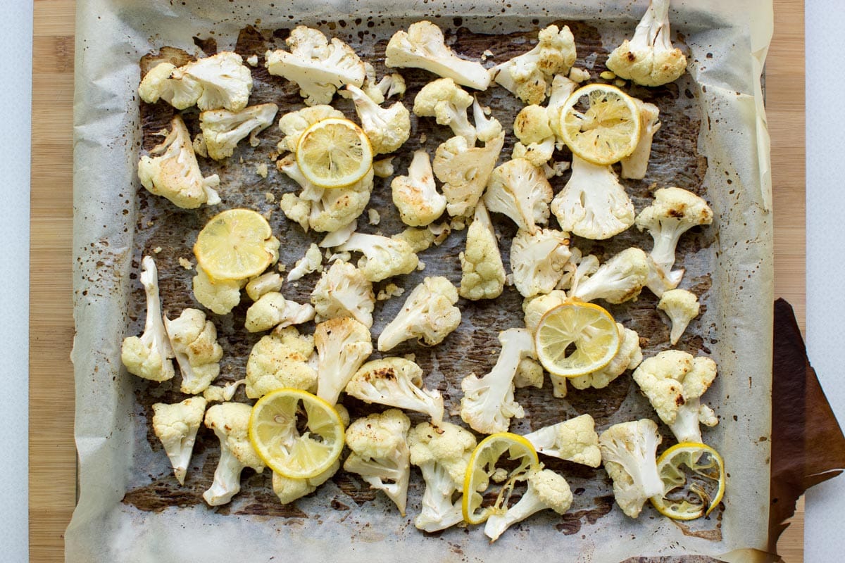 A baking sheet covered with parchment paper with baked cauliflower and lemon on a wooden surface | Hurry The Food Up