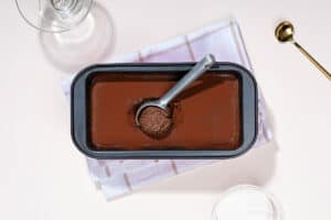 A black container with ice cream is on a towel beside a golden spoon and two glasses | Hurry The Food Up