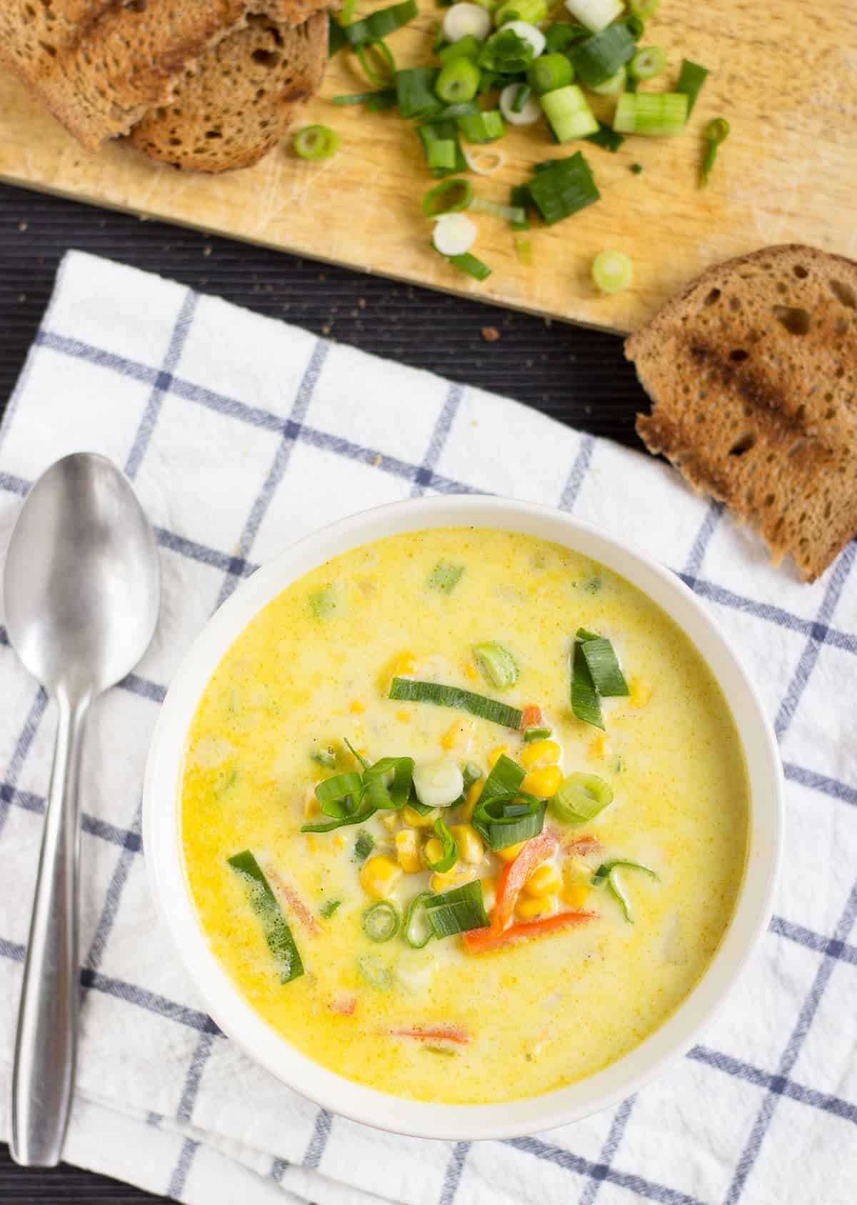 A bird’s eye view of a bowl of chowder, sprinkled with green onions, on a checked kitchen towel | Hurry The Food Up
