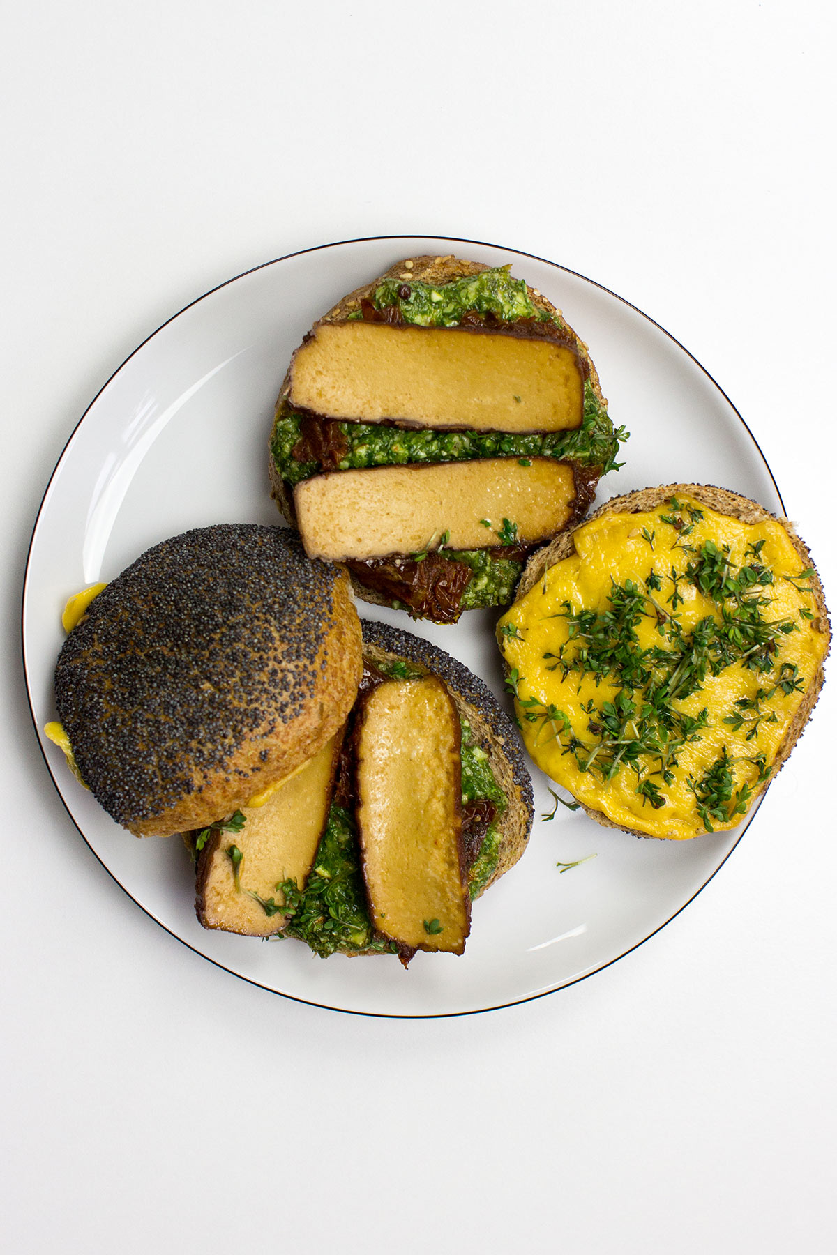 A Tofu Pesto Sandwich with crispy bread, layered with marinated tofu, fresh greens, and a generous spread of vibrant pesto, sits on a plate, ready to be enjoyed.