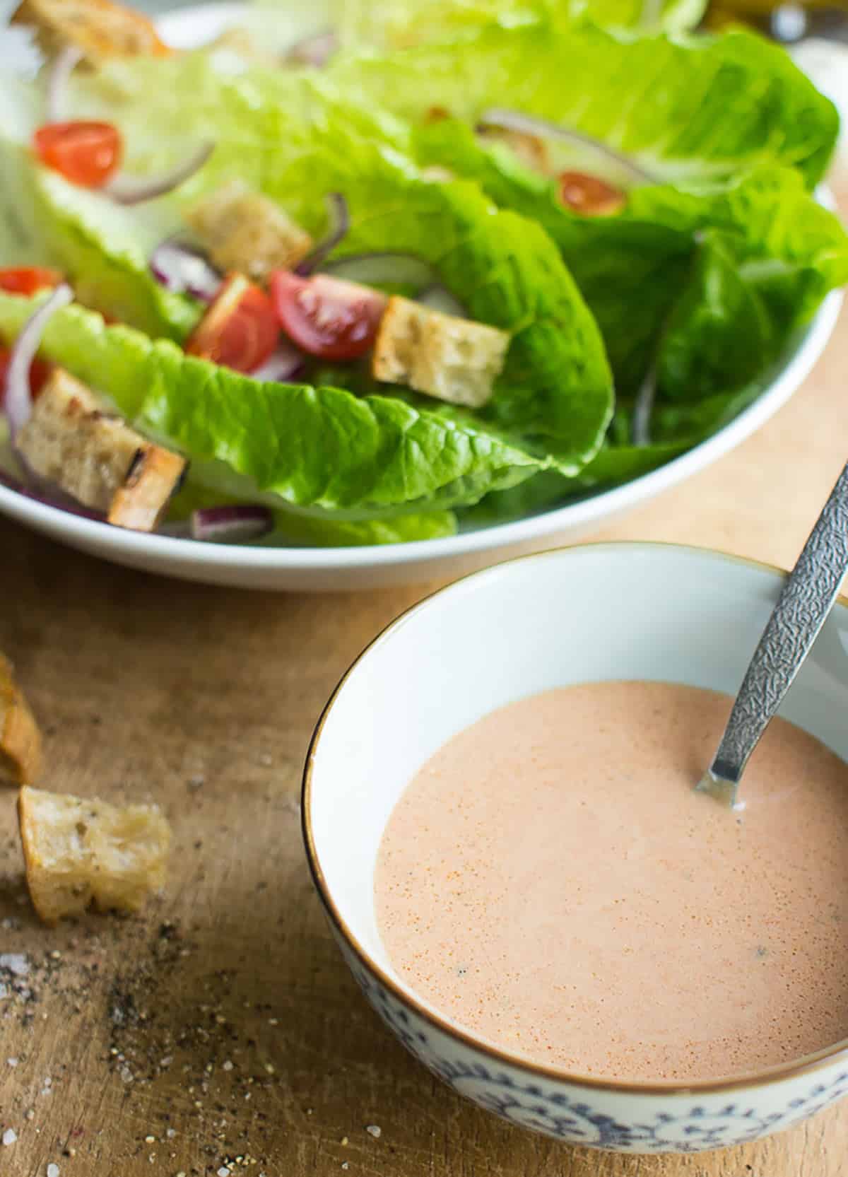 A bowl of vegan caesar dressing with a spoon in it. A plate of vegan caesar is nearby | Hurry The food Up
