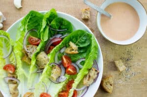 Vegan caesar salad is served on a plate, a bowl of salad dressing is nearby| Hurry The food Up