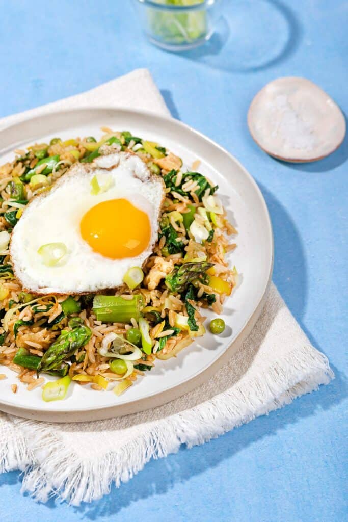 A plate of fried rice with a fried egg on top, a tray of salt next to it & a cup of spring onions | Hurry The Food Up