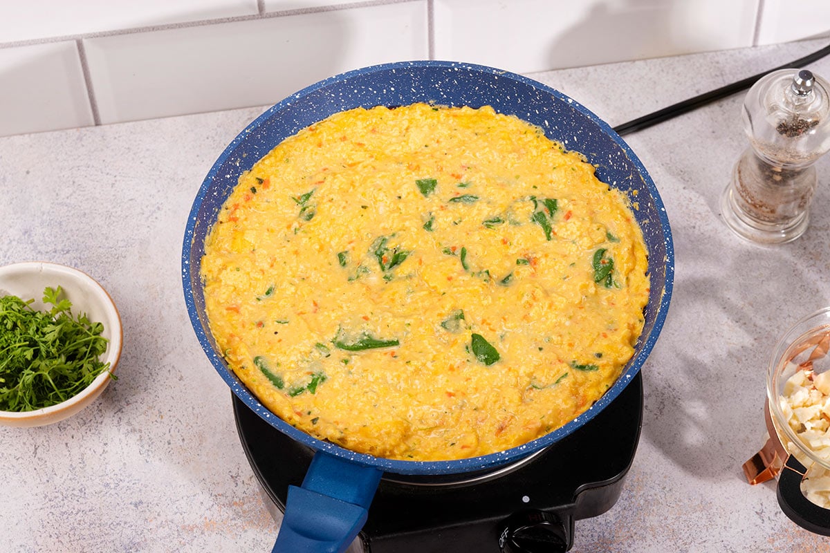 The egg mixture is cooking on the pan. There is a small bowl with herbs on the left and a bowl of crumbled fet and black pepper on teh right | Hurry The Food Up