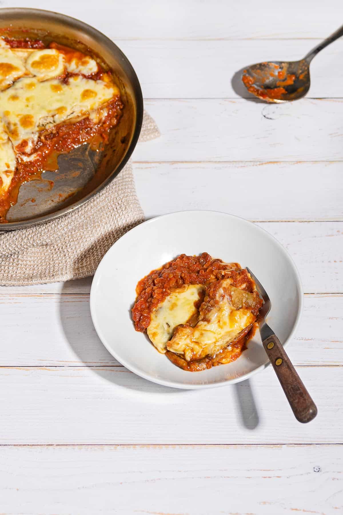 Vegetarian Moussaka is served in a plate with a tablespoon and a pan beside it | Hurry The Food Up
